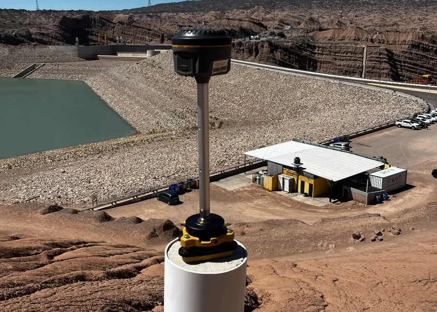 Receptor GNSS sobre un pilar de hormigón, con el paramento de una presa al fondo.
