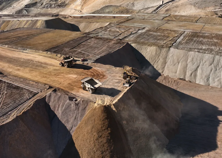 Vista aérea de camiones mineros descargando en el borde de una escombrera, con los bancos del avance al fondo.