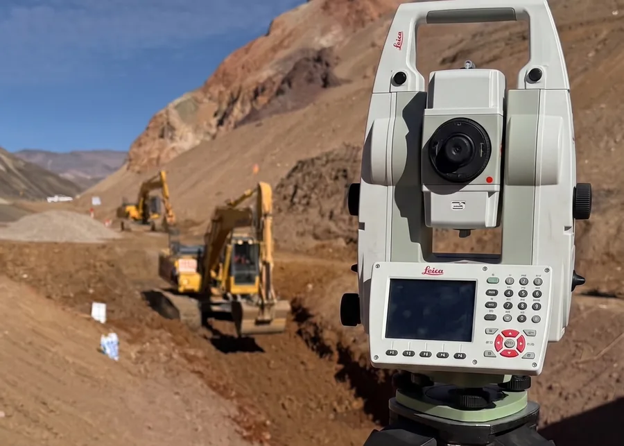 Estación total sobre la traza de un camino de montaña, con excavadoras trabajando.