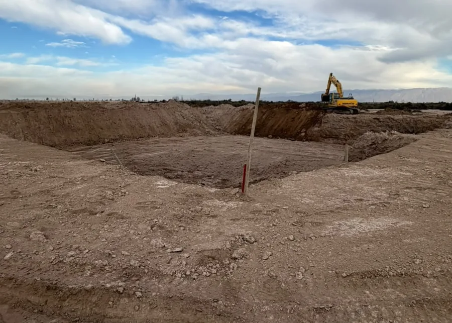 Excavación del vaso de un reservorio, con una excavadora trabajando al fondo.